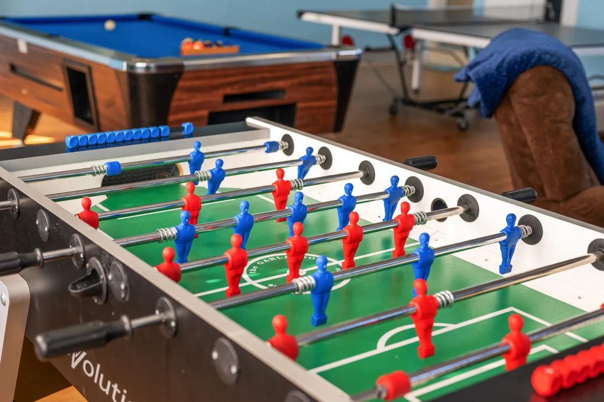 A dynamic entertainment area packed with a foosball table, pool table, ping pong table, and a comfortable chair. The room exudes energy and fun, with plenty of space for group tournaments or casual play sessions.