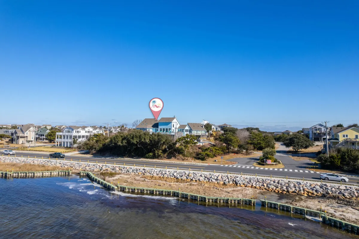 This exterior shot showcases a waterfront property with surrounding houses, a coastal road, and blue sky. It evokes the area’s family-friendly neighborhood, proximity to water, and opportunities for walking or biking to local attractions.