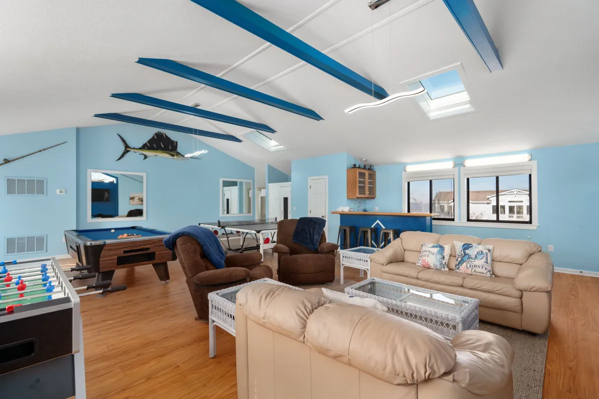 A lively entertainment room with a pool table, foosball table, blue accent beams, comfy seating area, and a bar counter—perfect for both spirited competition and relaxing with drinks. The inviting mood makes it ideal for group gatherings and movie nights.