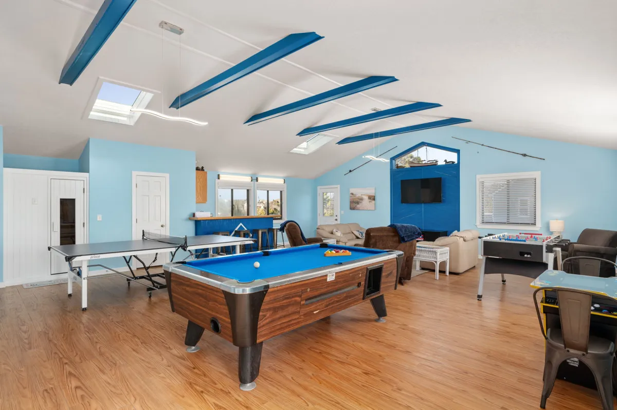 This bright and cheerful game room features a pool table and ping pong table as central attractions, with a sofa seating area for relaxing and large windows that fill the space with natural light. The overall mood is lively and social, making it an ideal backdrop for friendly competitions or laid-back movie nights.