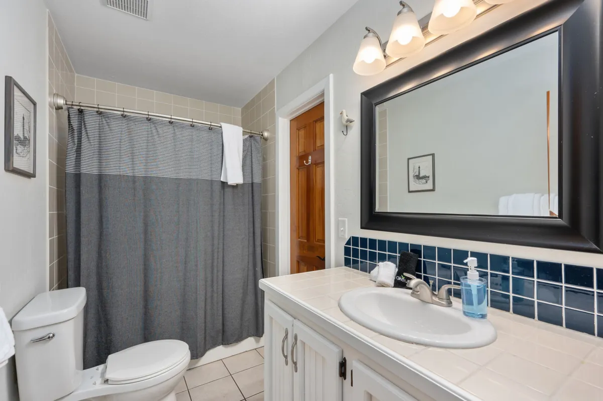 A pristine bathroom scene with a modern vanity, sink, mirror, bright towels, and a shower curtain. The space is tidy and inviting, suggesting a relaxing environment for personal care and winding down after a busy day.