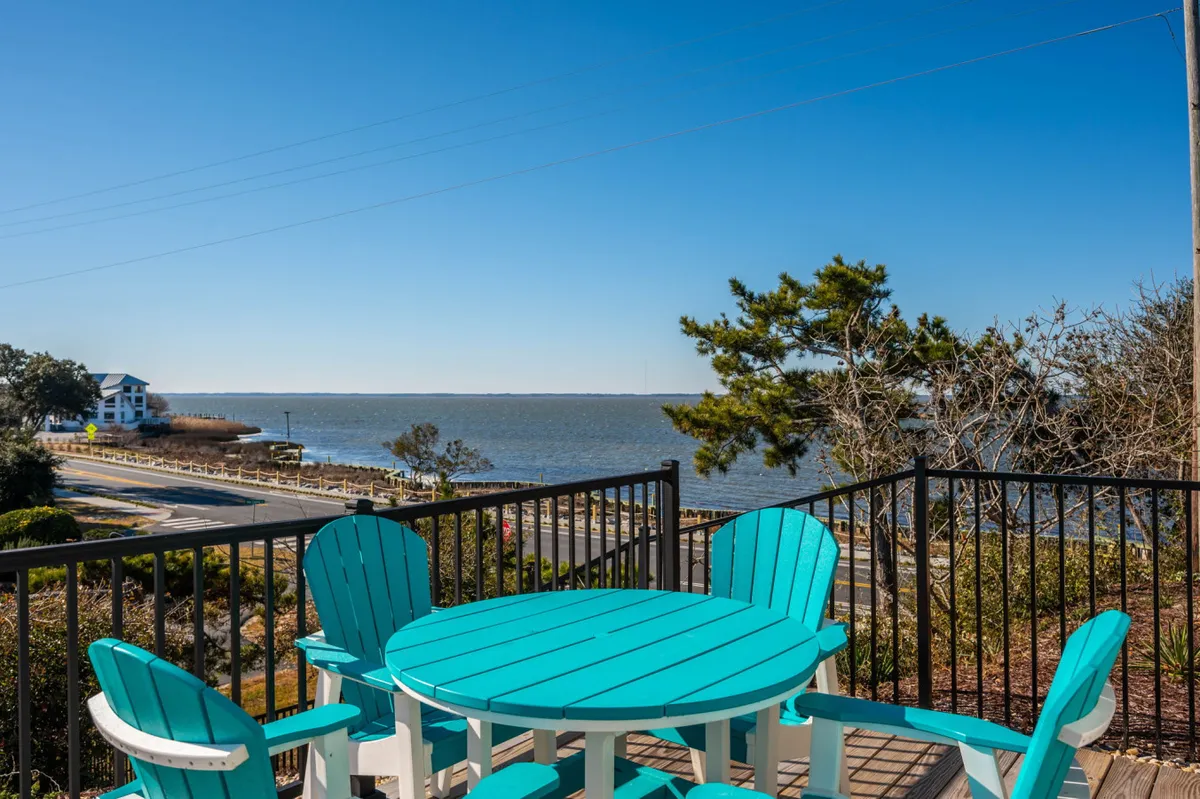 An inviting waterfront deck with turquoise outdoor furniture, offering unobstructed views of the sound. The setting sun casts a golden glow over the water, creating a serene and picturesque backdrop for gathering with friends or enjoying a quiet moment outdoors.