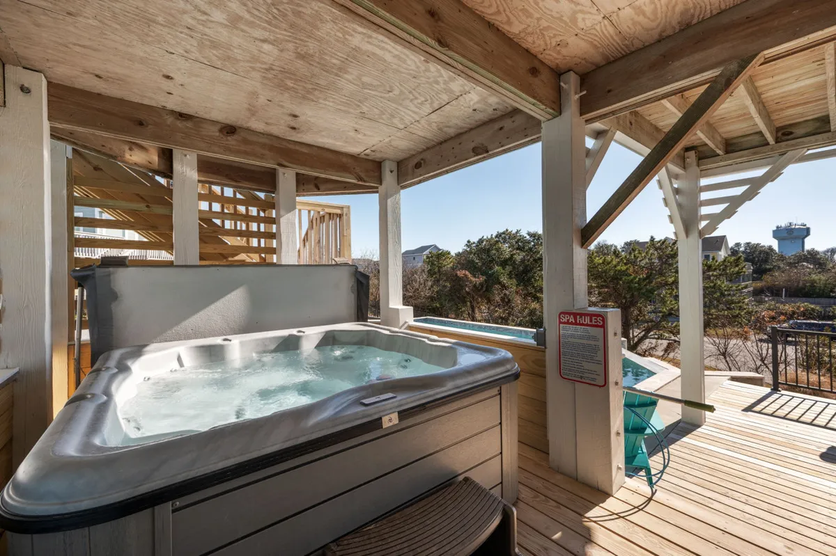 A secluded wooden deck features a luxurious hot tub overlooking a scenic, tranquil landscape. The open-air environment is perfect for relaxing under the stars or unwinding after an adventurous beach day.