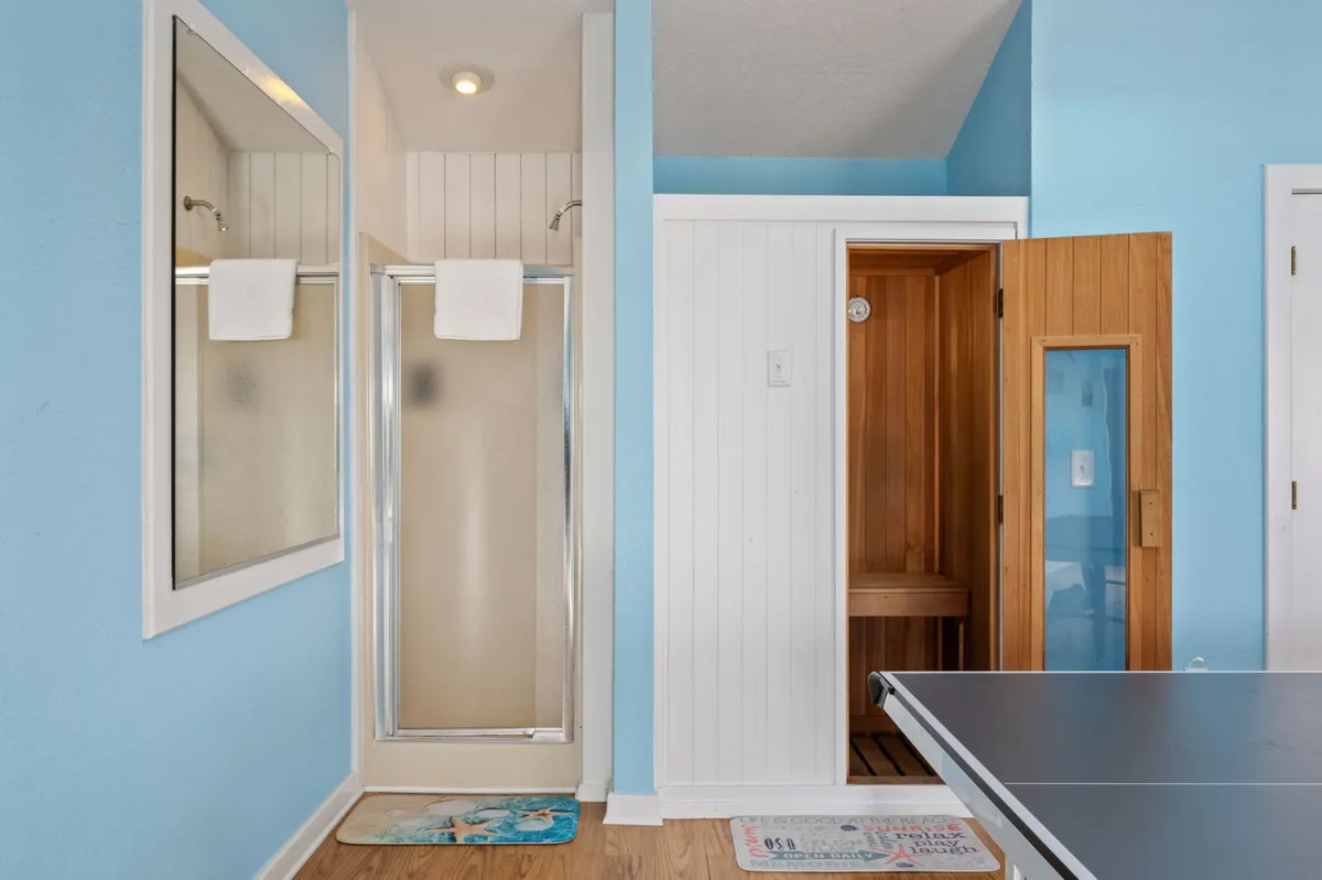 A serene wellness area with a modern shower and a wooden sauna, complemented by a mirrored wall. The calming mood creates the perfect spot for restful moments after the excitement of the game room.