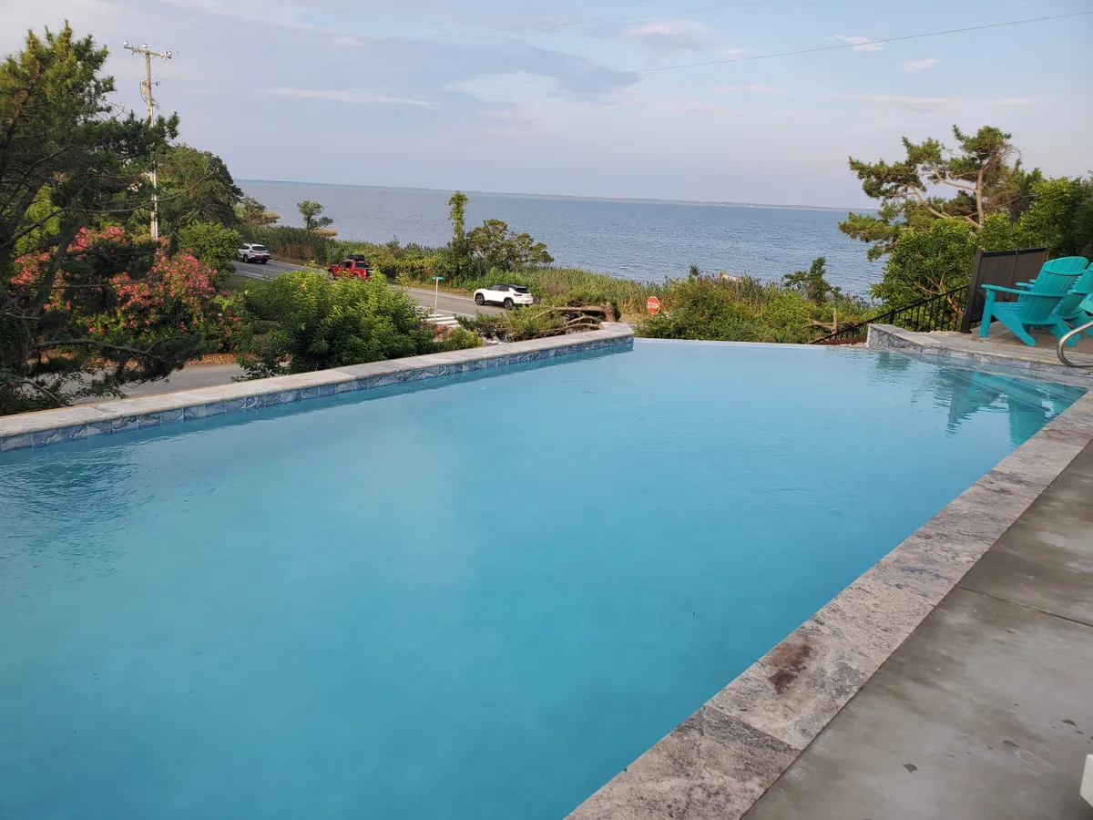 This image captures a serene exterior scene featuring an infinity pool overlooking the ocean, surrounded by greenery and lounge chairs. The pool and expansive view set a scene of relaxation and family fun outdoors.