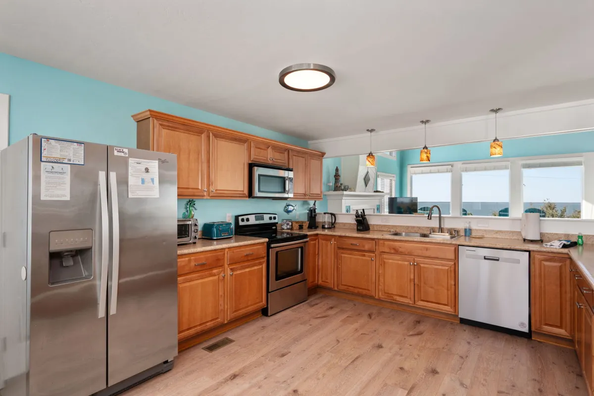 A beautifully lit kitchen featuring stainless steel appliances, wooden cabinetry, a central kitchen island, and large windows with scenic views. The space feels both functional and welcoming, perfect for meal prep and casual gatherings.